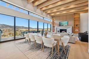 Dining room with built in shelves, a fireplace, beamed ceiling, and light wood-style flooring