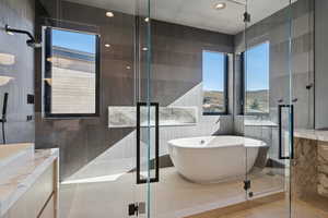 Bathroom featuring tile walls, vanity, plenty of natural light, a soaking tub, and a tile shower