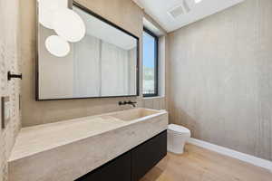 Bathroom with wallpapered walls, light wood finished floors, and vanity