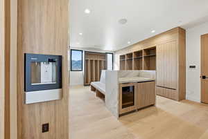 Kitchen with modern cabinets, open shelves, wine cooler, light stone countertops, and light wood-type flooring