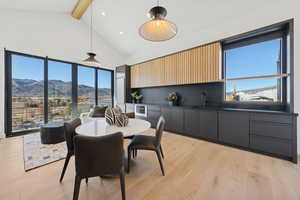 Dining area featuring a mountain view, beam ceiling, high vaulted ceiling, light wood finished floors, and plenty of natural light