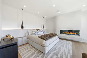 Bedroom with a glass covered fireplace, recessed lighting, and light wood-type flooring