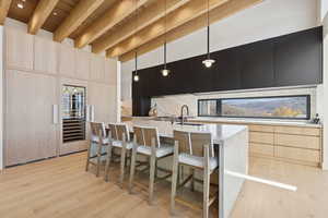 Kitchen featuring light brown cabinets, modern cabinets, dark cabinets, a kitchen bar, and light stone counters