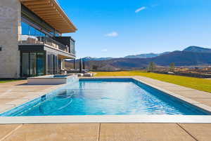 View of swimming pool featuring a mountain view, a balcony, a lawn, a patio area, and a pool with connected hot tub