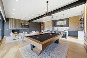 Playroom with pool table, light wood-style flooring, recessed lighting, a warm lit fireplace, and an accent wall