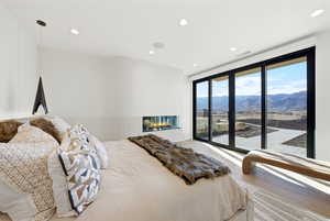 Bedroom with a mountain view, access to exterior, wood finished floors, recessed lighting, and a glass covered fireplace