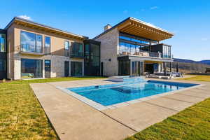 Back of property featuring a balcony, a lawn, a patio area, and a pool with connected hot tub