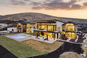 Back of property at dusk featuring stairs, a balcony, a patio, and a yard