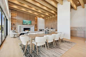 Dining area with built in shelves, light wood-style flooring, a high end fireplace, and a wood ceiling with exposed beams