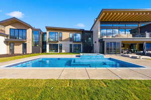 Back of property with a balcony, a patio, a pool with connected hot tub, and a lawn