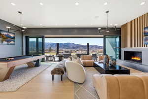 Living area featuring pool table, a mountain view, a lit fireplace, wood finished floors, and plenty of natural light