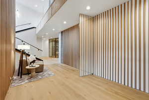 Hallway featuring recessed lighting, light wood-style flooring, a high ceiling, an accent wall, and stairway