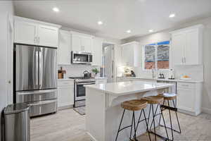 Kitchen featuring stainless steel appliances, a kitchen bar, tasteful backsplash, white cabinets, and recessed lighting