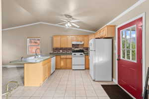 Kitchen featuring white appliances, plenty of natural light, vaulted ceiling, light brown cabinets, and crown molding