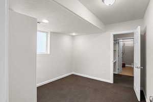 Basement with a textured ceiling, dark colored carpet, and a textured wall