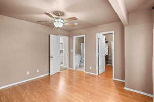 Unfurnished bedroom with a walk in closet, light wood finished floors, ceiling fan, connected bathroom, and beamed ceiling