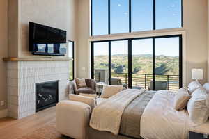 Bedroom featuring access to exterior, wood finished floors, a tile fireplace, and a high ceiling