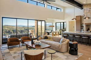 Living room featuring a mountain view, ceiling fan, light wood-style flooring, beamed ceiling, and a towering ceiling