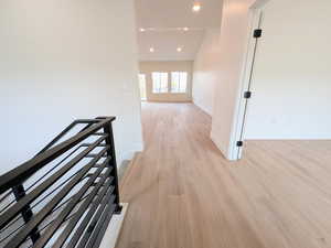 Hall with an upstairs landing, light wood finished floors, and recessed lighting