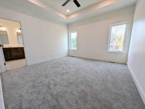 Unfurnished bedroom with a tray ceiling, light carpet, a ceiling fan, ensuite bath, and recessed lighting