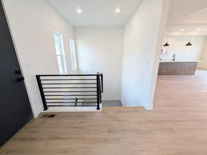 Corridor with light wood-type flooring, recessed lighting, and an upstairs landing