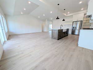 Kitchen featuring open floor plan, white cabinets, hanging light fixtures, light wood-type flooring, and stainless steel refrigerator with ice dispenser