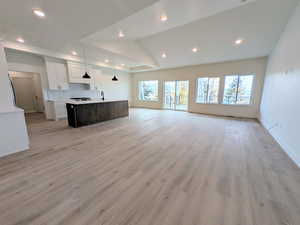 Unfurnished living room with vaulted ceiling, light wood-style floors, and recessed lighting