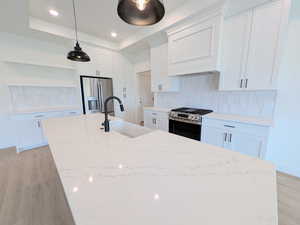 Kitchen featuring light wood finished floors, light stone counters, backsplash, white cabinetry, and recessed lighting