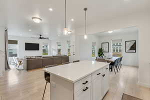 Kitchen featuring white cabinets, a breakfast bar, hanging light fixtures, open floor plan, and a center island