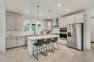 Kitchen with stainless steel appliances, pendant lighting, a breakfast bar, a kitchen island, and wall chimney range hood