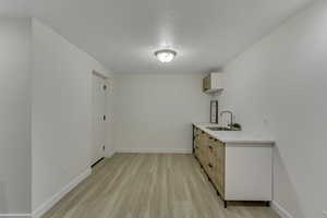 Kitchen featuring light wood finished floors, light brown cabinetry, light stone countertops, a textured ceiling, and modern cabinets