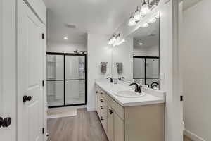 Full bath with a shower stall, double vanity, and light wood-type flooring