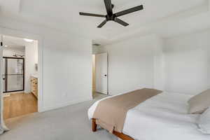 Bedroom featuring light carpet, ceiling fan, connected bathroom, and a tray ceiling