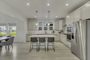 Kitchen with appliances with stainless steel finishes, decorative light fixtures, white cabinets, a breakfast bar area, and recessed lighting