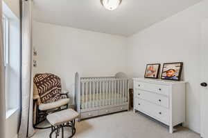 Bedroom featuring light colored carpet and a nursery area