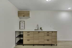 Bar area with light brown cabinetry, modern cabinets, light wood-type flooring, and light stone counters