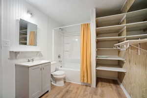 Bathroom with light wood-type flooring, shower / bathtub combination with curtain, vanity, and wooden walls
