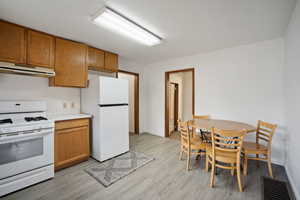Kitchen with white appliances, light countertops, brown cabinets, under cabinet range hood, and light wood-type flooring