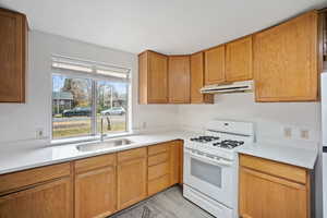 Kitchen featuring white gas range oven, under cabinet range hood, light wood-style floors, brown cabinetry, and light stone counters
