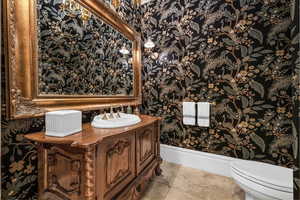 Half bathroom with wallpapered walls, vanity, and light tile patterned flooring
