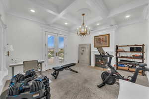 Workout room featuring beam ceiling, carpet floors, coffered ceiling, a fireplace with flush hearth, and ornamental molding