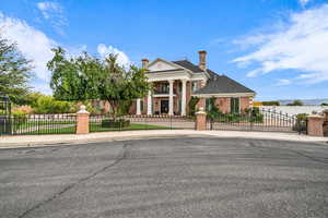Greek revival inspired property with a fenced front yard, a chimney, brick siding, and a gate