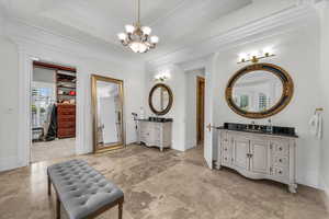 Bathroom with ornamental molding, two vanities, a walk in closet, a chandelier, and a raised ceiling