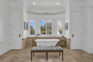 Bathroom featuring wainscoting, tile walls, ornamental molding, and a freestanding tub