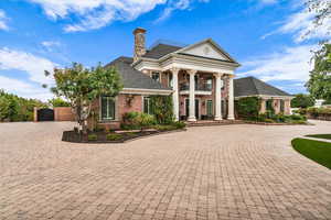 Greek revival inspired property featuring curved driveway, brick siding, a chimney, a gate, and covered porch