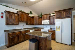 Kitchen with dark countertops, white appliances, lofted ceiling, a center island, and dark brown cabinets