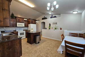 Kitchen featuring dark brown cabinets, arched walkways, vaulted ceiling, white appliances, and a kitchen island