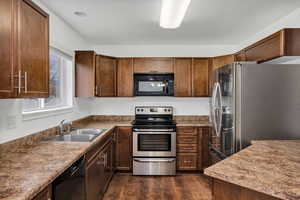 Kitchen with black appliances, dark wood-type flooring, and dark stone countertops