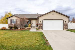 Ranch-style house with stone siding, concrete driveway, a shingled roof, an attached garage, and a gate