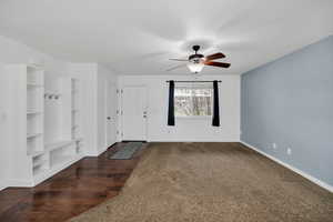 Mudroom with built in shelves, dark colored carpet, dark wood-style flooring, and ceiling fan